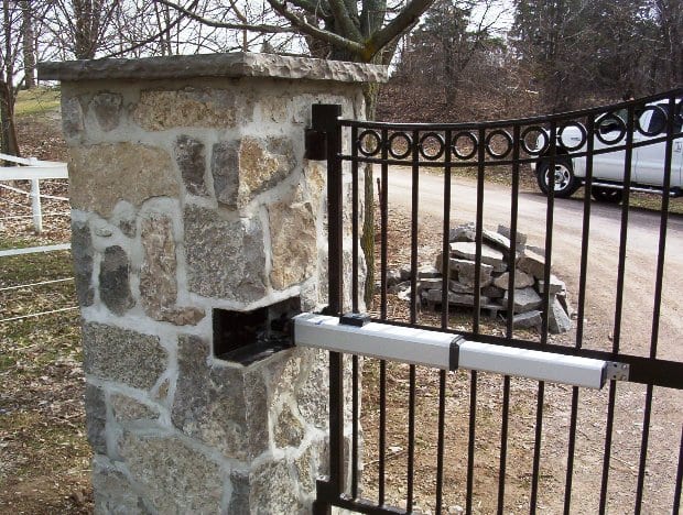 Hydraulic gate opener on ornamental iron gate with stone column